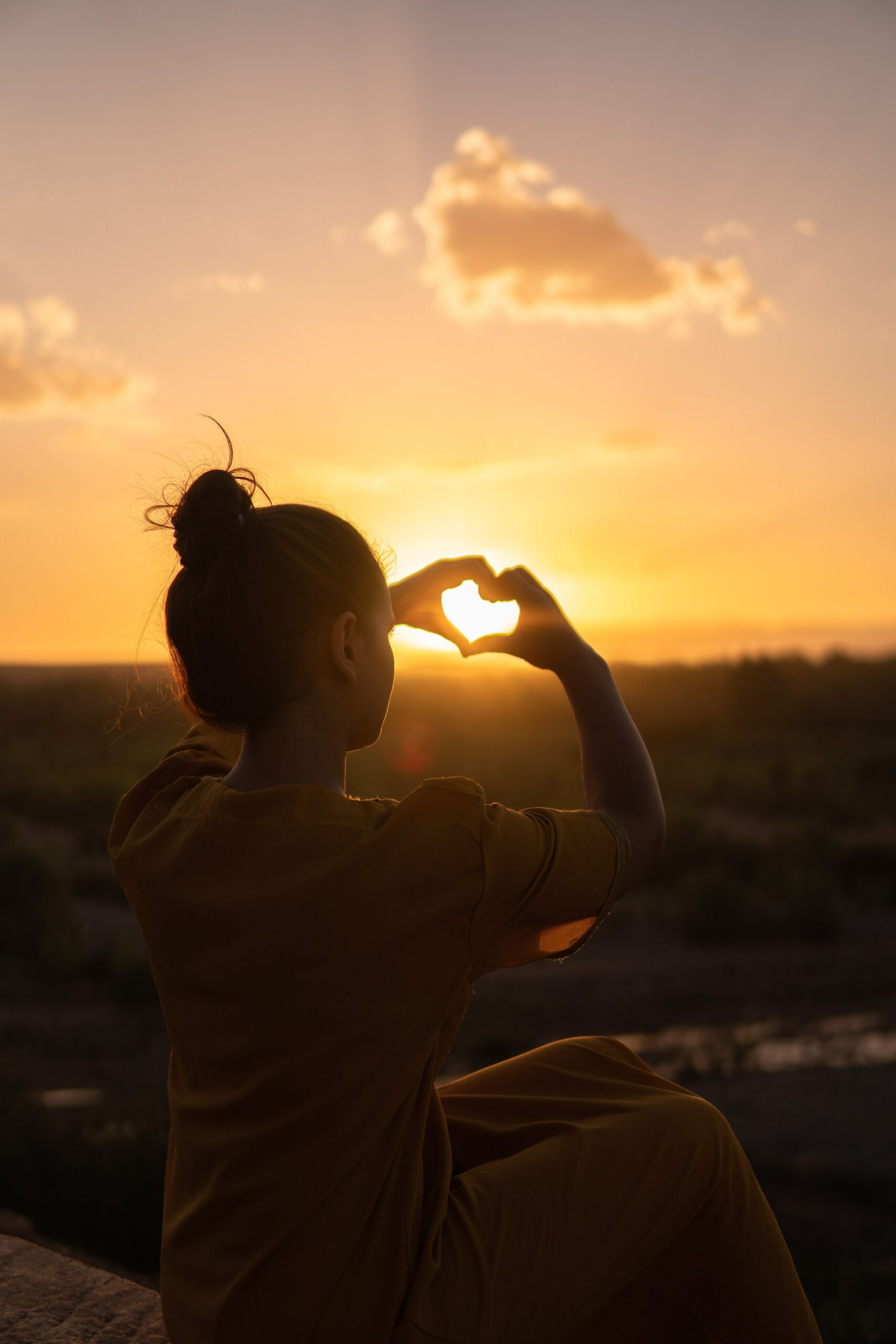 A woman is using physical therapy techniques to make a heart shape with her hands at sunset.