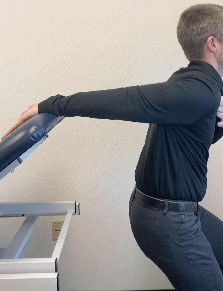 A man performing a shoulder stretch as part of physical therapy in an office.