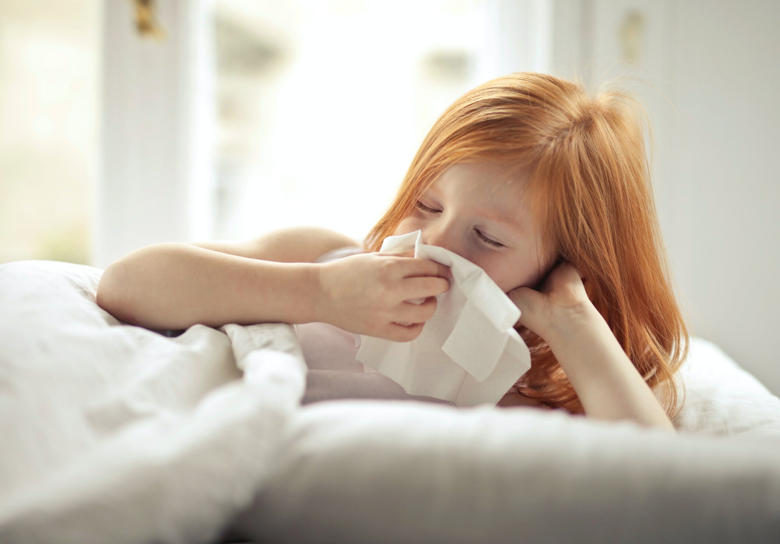 A little girl receiving physical therapy while blowing her nose in bed.