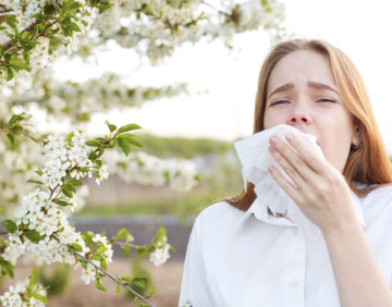 A woman undergoing physical therapy gently blows her nose amidst a vibrant flowering tree.